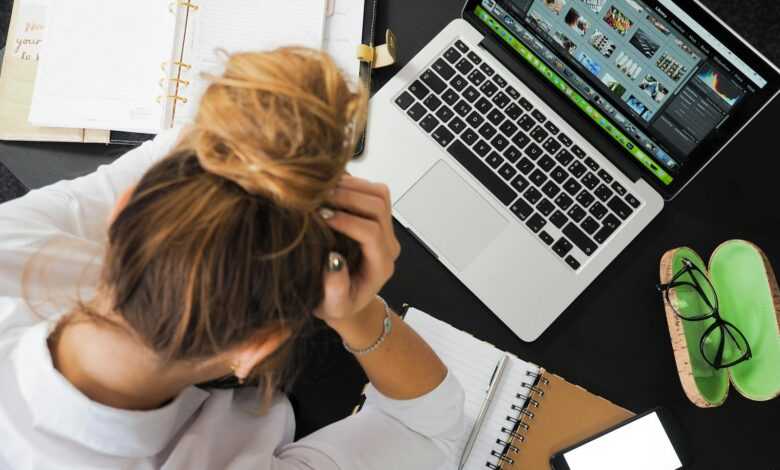 Overhead view of a stressed woman working at a desk with a laptop, phone, and notebooks.